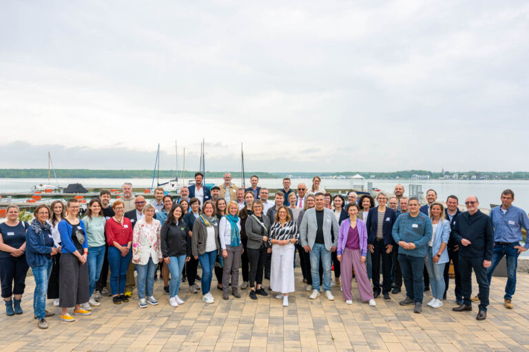 Teilnehmer der ZukunftSchmiede live haben sich zum Gruppenfoto versammelt. Im Hintergrund ist der Hainer See zu sehen