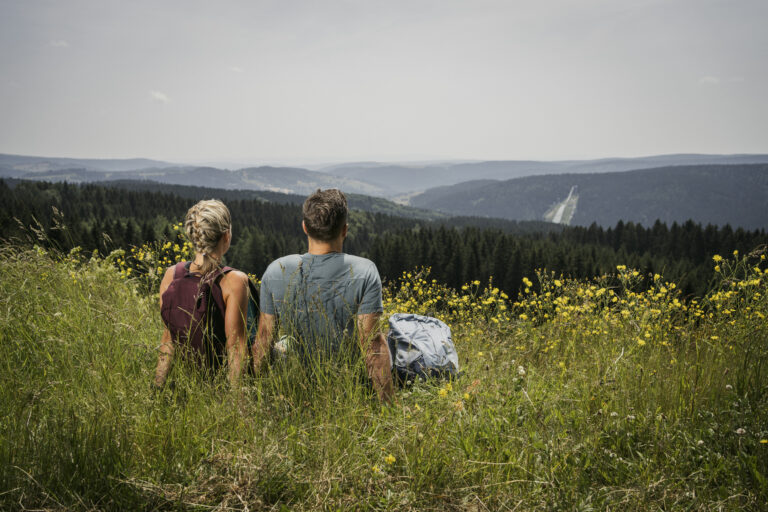 Ein Mann und eine Frau sitzen in einer grünen Landschaft und schauen vom Kammweg aus auf die Natur ins Erzgebirge